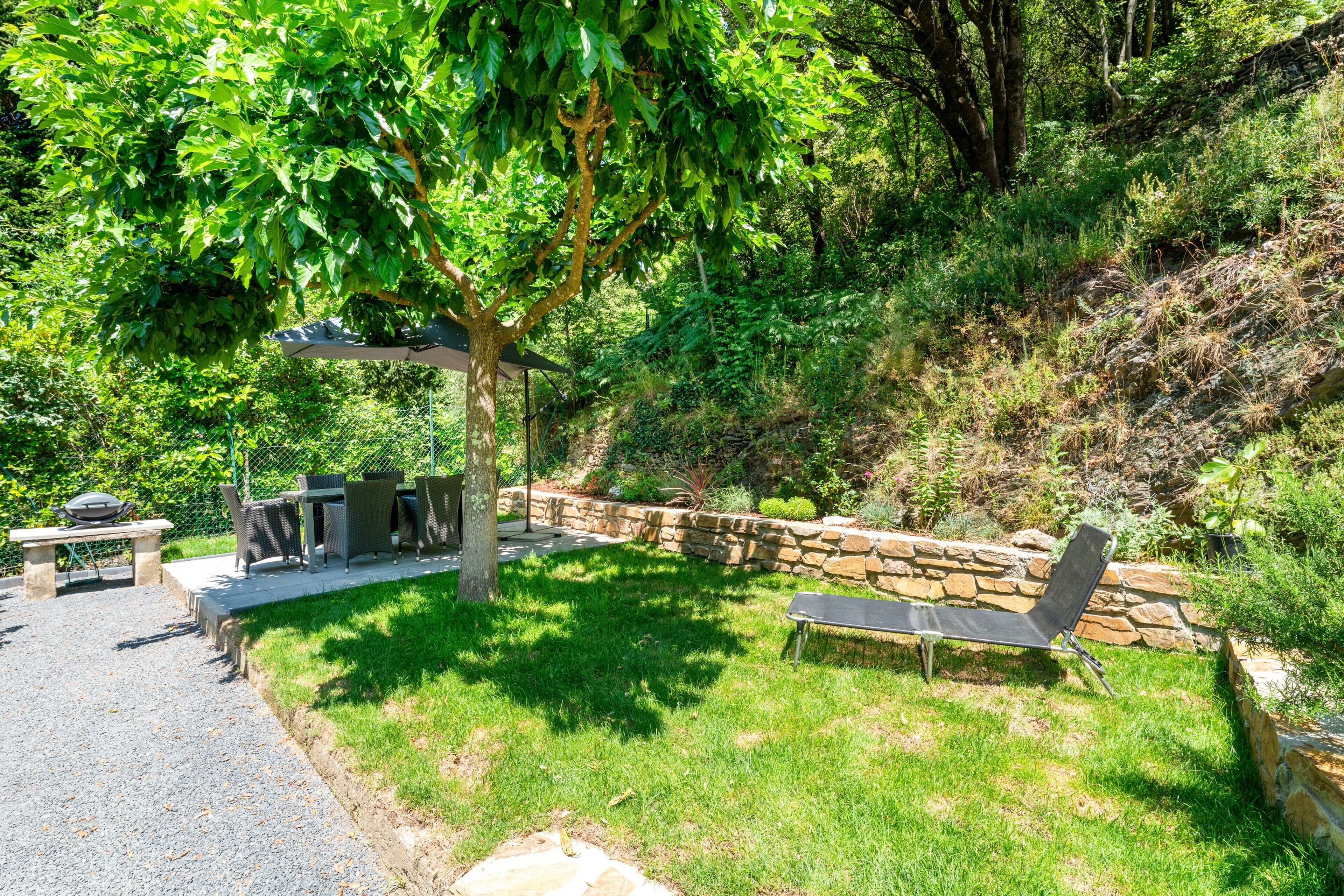 Zona de pati amb paret de pedra, una barbacoa i mobles d'exterior.