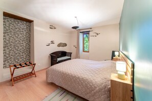 A bedroom with a bed, a wooden nightstand, a lamp, a bench, a window, and a wall with decorative elements.