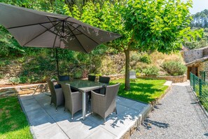 An outdoor patio with a table and chairs, a large umbrella, and a stone wall.