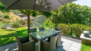 Een terras buiten met een tafel, stoelen, een barbecue en een stenen muur op de achtergrond.