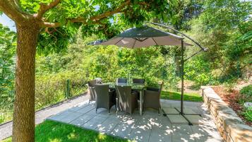 An outdoor patio with a table and chairs, a grill, and a pergola with an umbrella.
