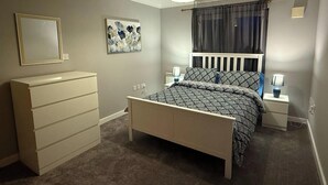Ein Schlafzimmer mit Bett, Nachttischen, einer Kommode, einer Pendelleuchte und einem Bild an der Wand.