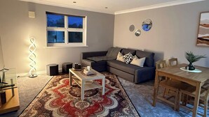 Ein Wohnzimmer mit Sofa, Couchtisch, Teppich, Esstisch, Stühlen und einem Fenster.