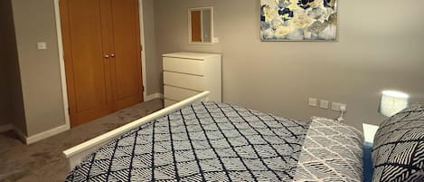 Un dormitorio con una colcha estampada, un armario de madera, un tocador y un espejo, además de un cuadro en la pared.