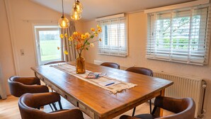 Une salle à manger avec une table en bois, six chaises, un vase de fleurs et des luminaires suspendus.