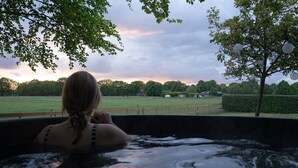Une personne se détend dans un bain à remous, avec vue sur un champ verdoyant et des arbres.