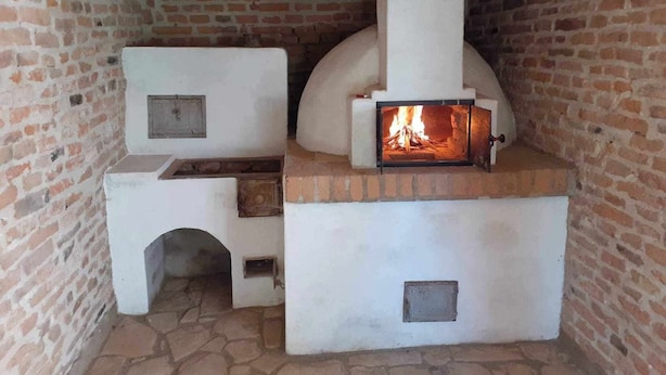 A traditional brick oven with a fire burning inside, a white chimney, and a stone floor.