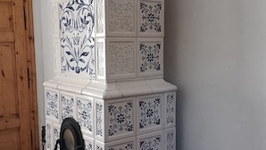 A traditional stove with intricate black and white tile patterns, a wooden door, and a rustic wooden table with a pot and a fur rug.