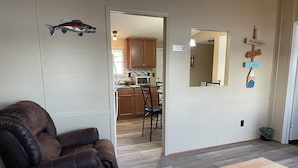 A living room with a brown leather chair, a wooden coffee table, and a remote control on it. There is a kitchen visible through an open doorway. - 3-bedroom home on beautiful Lake Greenwood, close to Old Eight Golf Course. (Waterloo)