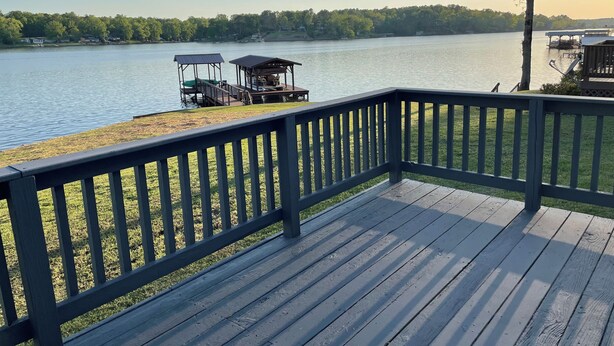 A wooden deck with a railing overlooking a lake, a dock with a covered structure, and a tree to the right. - 3-bedroom home on beautiful Lake Greenwood, close to Old Eight Golf Course. (Waterloo)