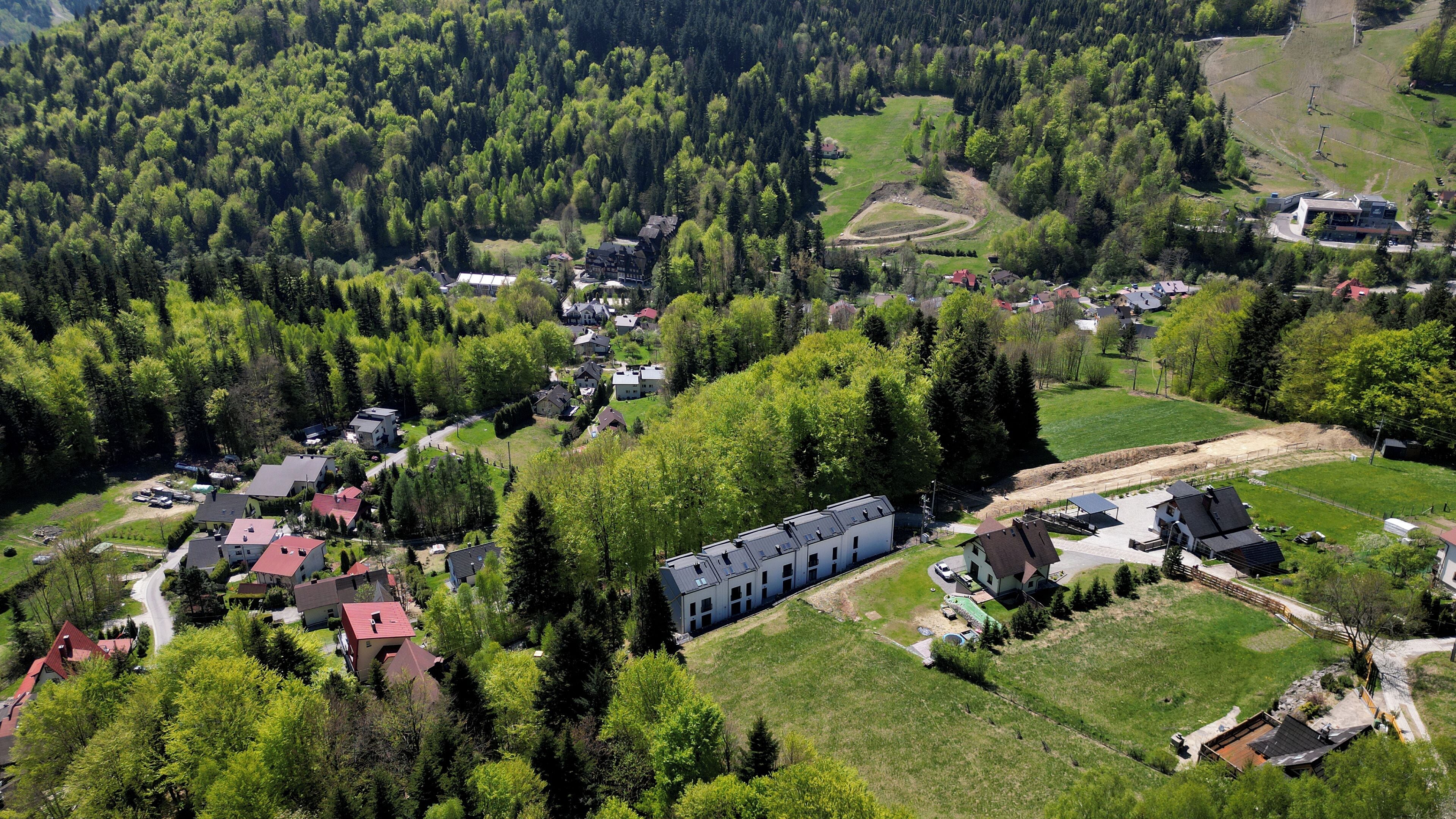 Vista aérea de un área residencial con casas, un edificio grande con múltiples ventanas y abundante vegetación.