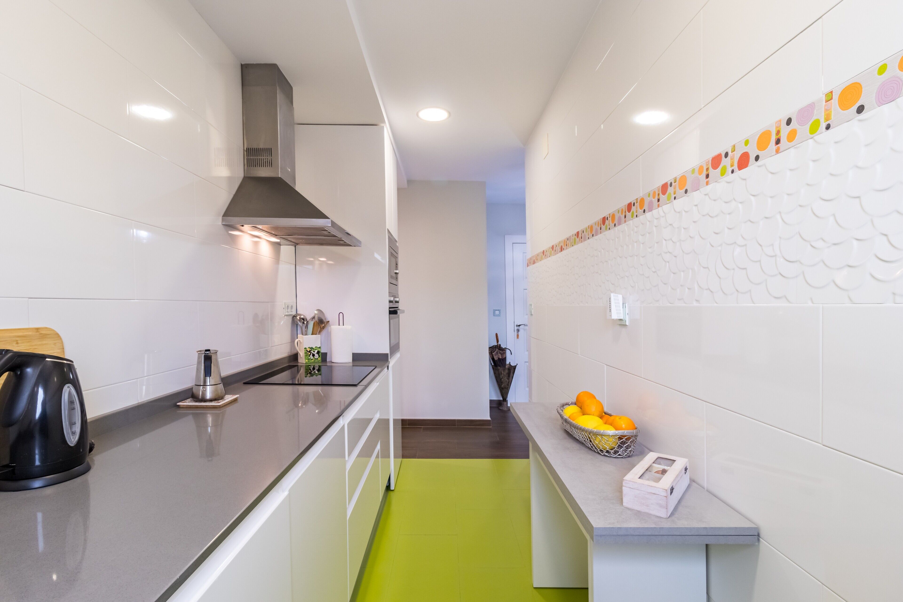 A modern kitchen with a stainless steel range hood, a kettle, and a fruit basket on the counter.