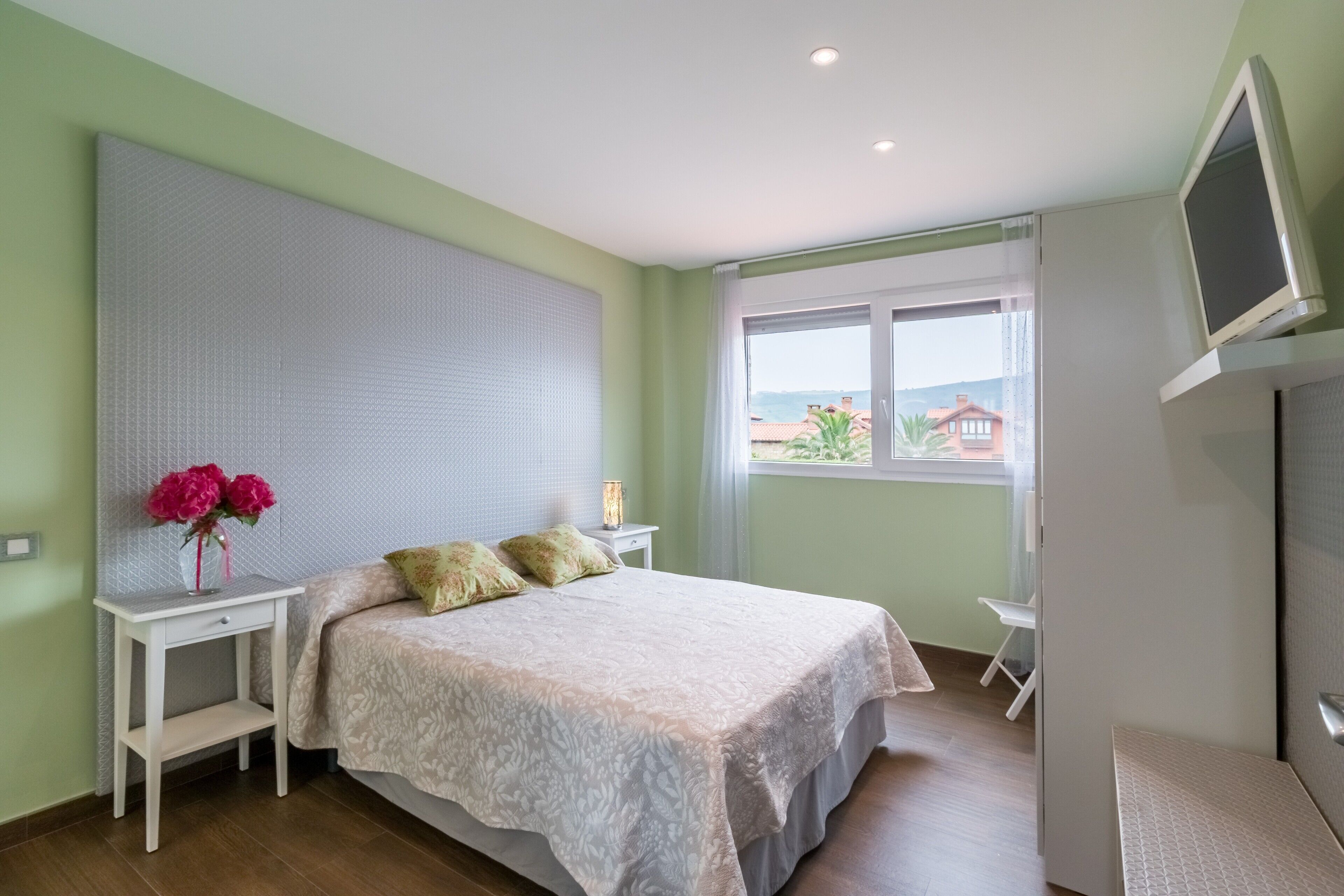 A bedroom with a bed, bedside table, lamp, and a TV.