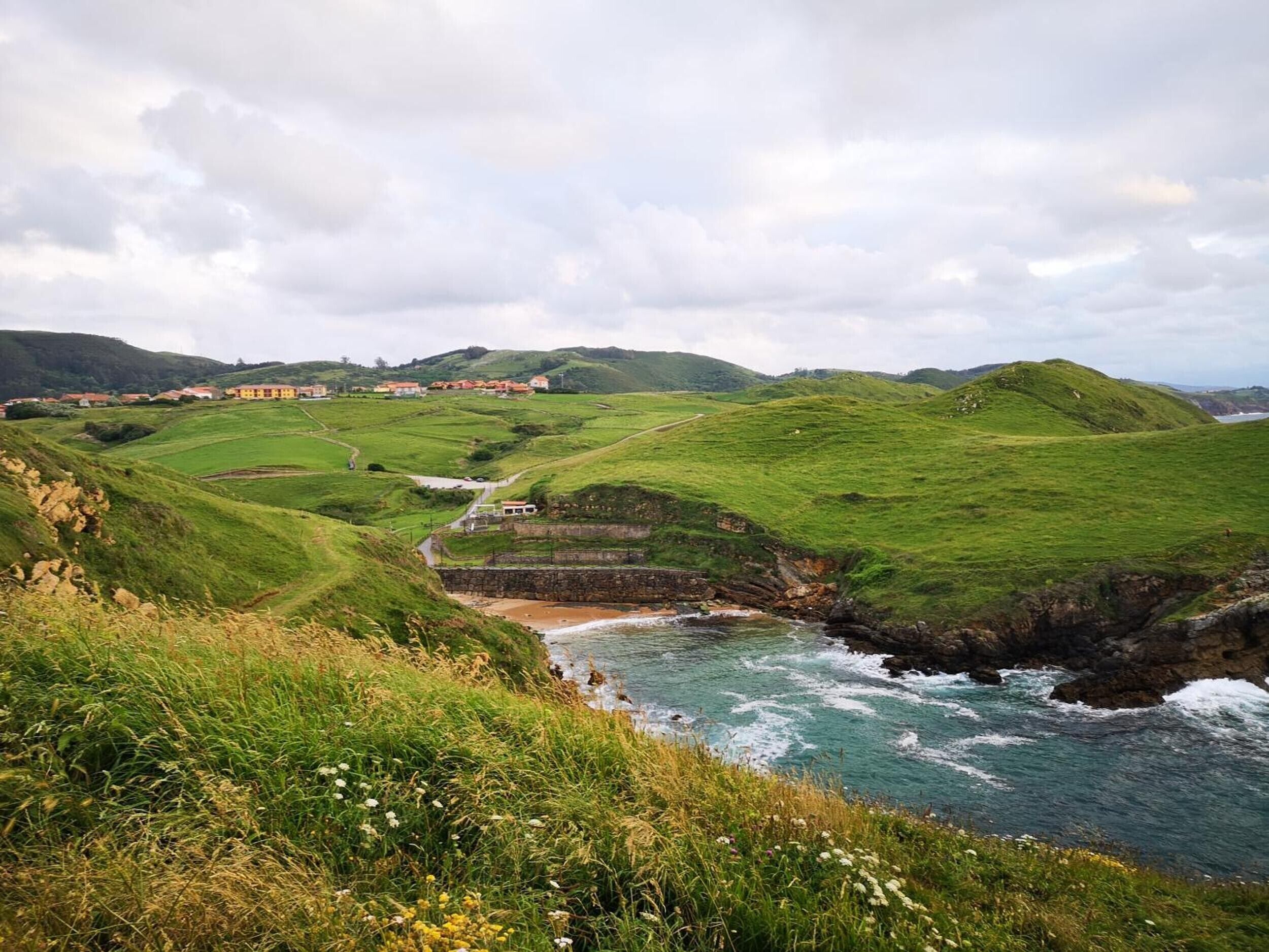 A coastal landscape with rolling hills, a stone bridge, and a distant village.