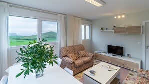 A living room with a sofa, TV, and a dining table with a plant. - Apartment 'Gloria-Patchwork' with Sea View, Shared Garden and Wi-Fi (Ubiarco)