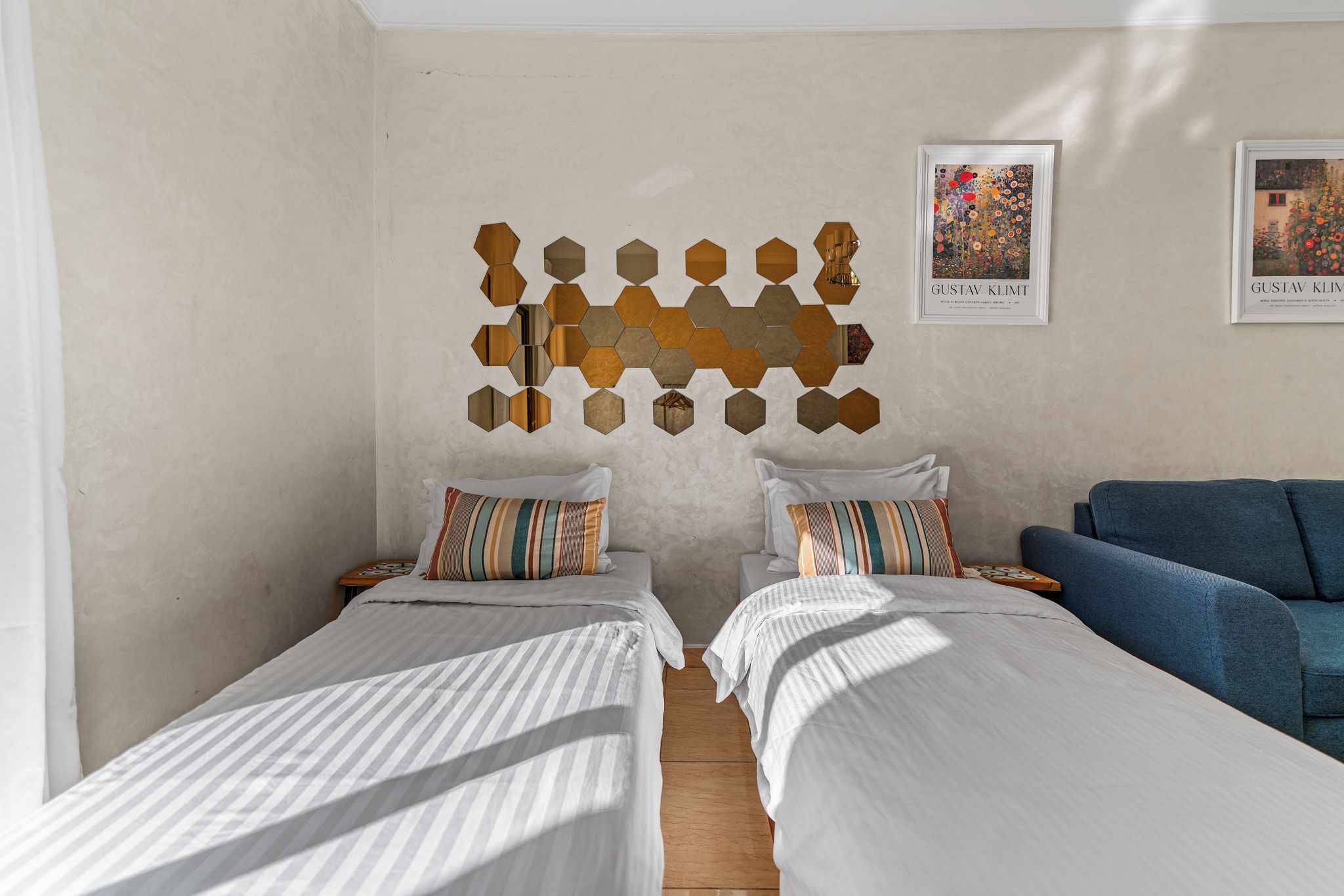 A hotel room with two single beds, a blue sofa, and a wall art piece.