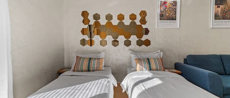 Une chambre d’hôtel avec deux lits simples, un canapé bleu et une œuvre d’art murale.