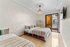 A hotel room with a bed, a bedside table, a wardrobe, a hanging light fixture, and a view of the outside. - Massira Social Living (Saâda)