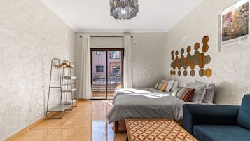 Ein Schlafzimmer mit Bett, Sofa, Pendelleuchte, Wandbild und Blick durch eine Tür.