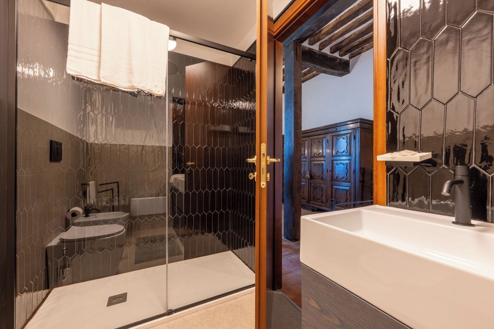 Un baño moderno con cabina de ducha de vidrio, un lavabo blanco y un mueble de madera al fondo.
