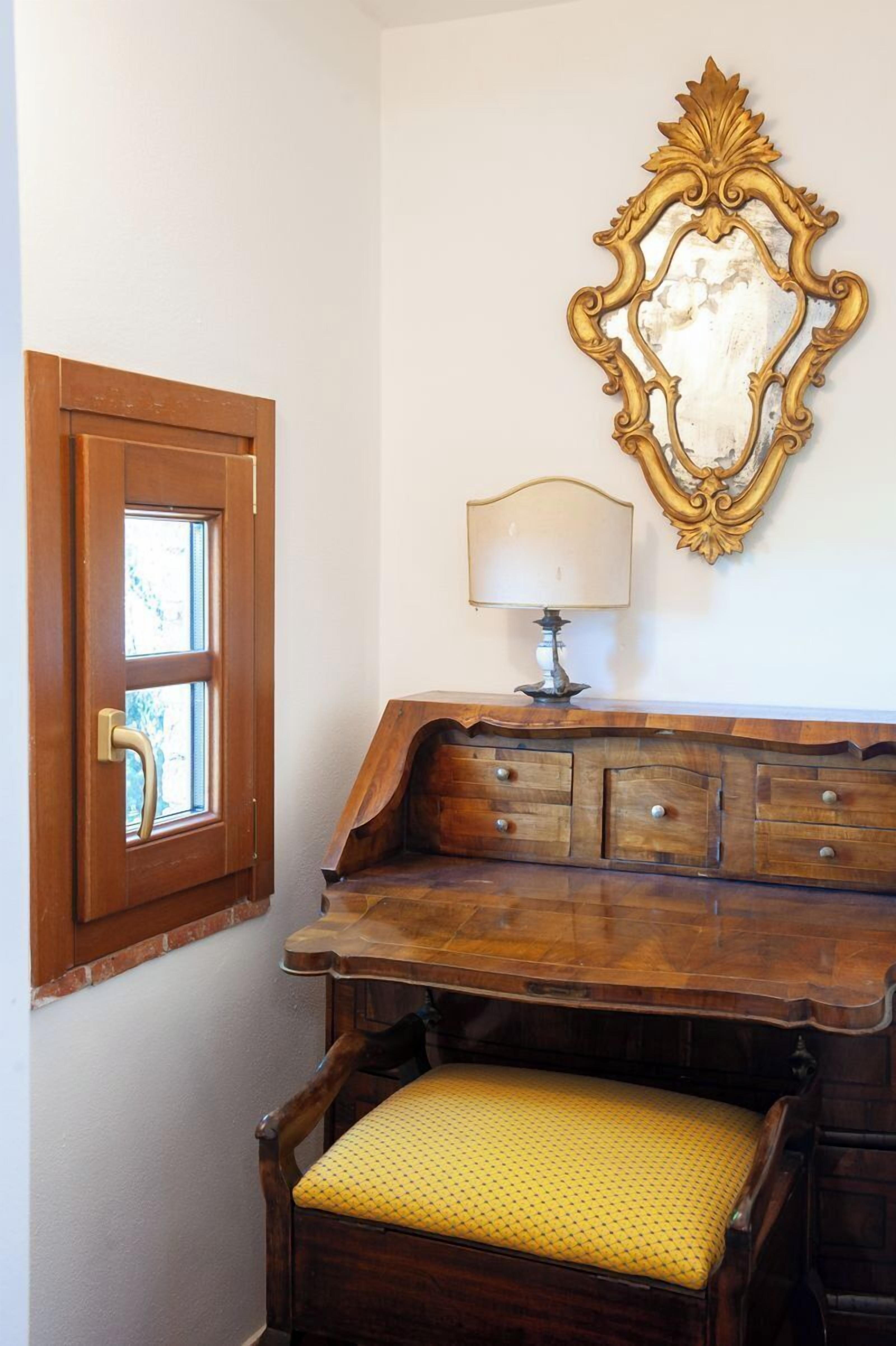 A wooden desk with drawers, a lamp, and a chair with a yellow cushion.