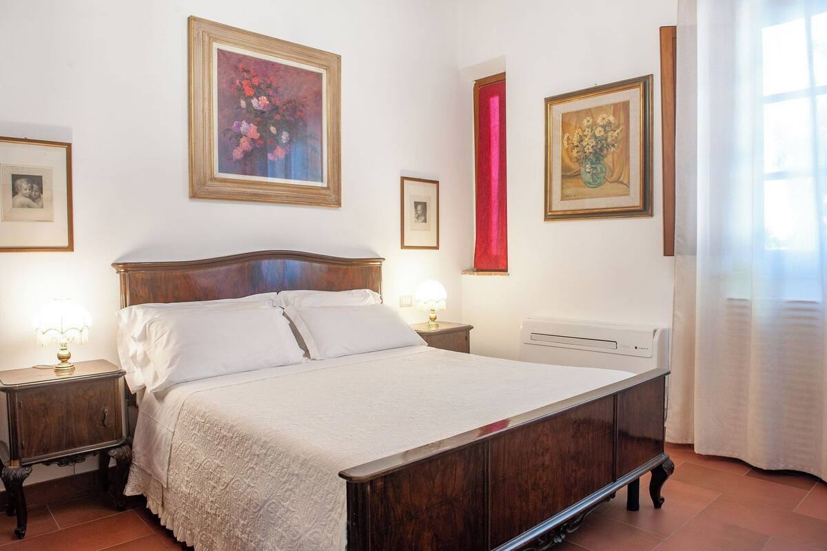 A bedroom with a wooden bed, two bedside tables with lamps, a radiator, and three framed pictures on the walls.