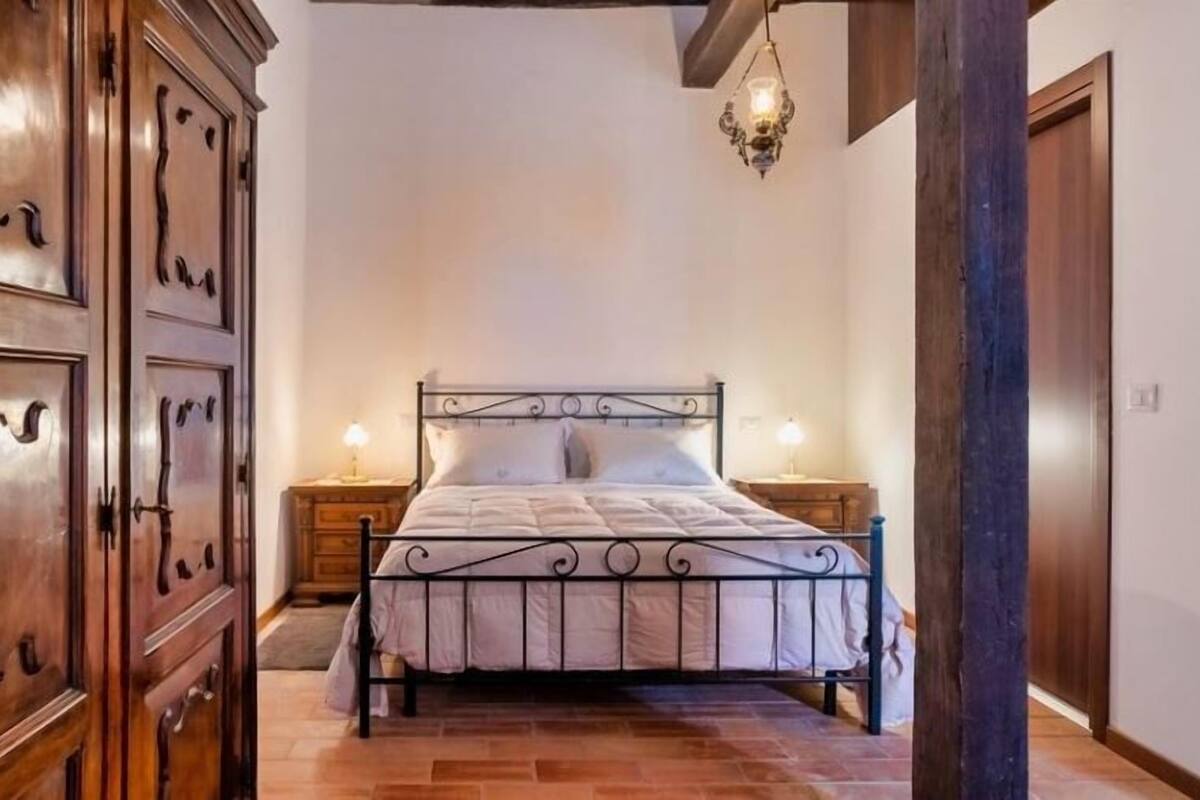 A bedroom with a bed, wooden wardrobe, and a hanging light fixture.