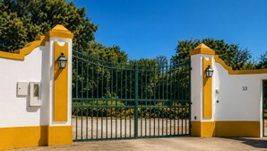 Une entrée fermée par un portail, avec le chiffre « 33 » inscrit sur le mur, un portail vert et une façade d’immeuble jaune et blanche.