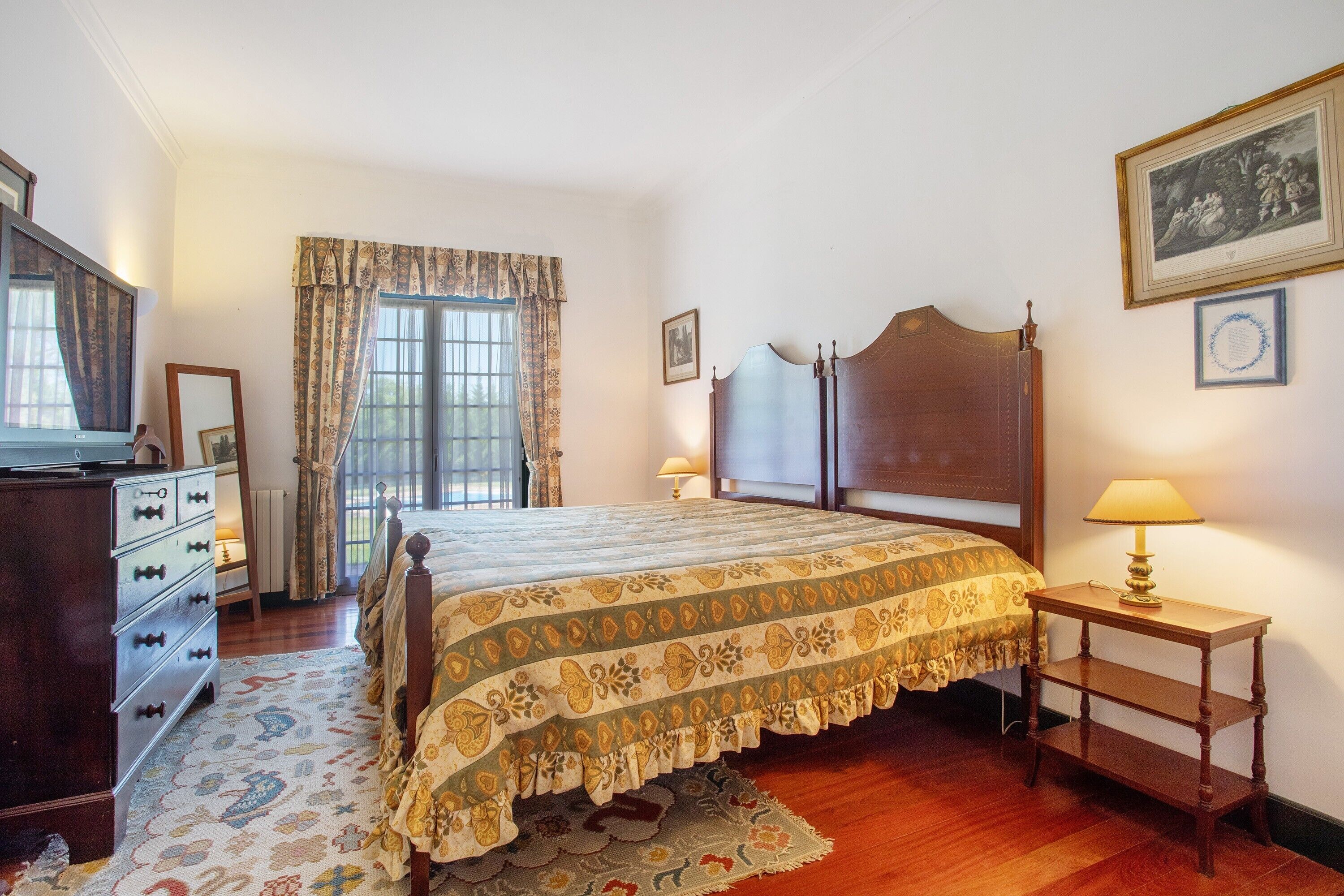 A bedroom with a bed, dresser, bedside table, lamp, window with curtains, and wall decorations.