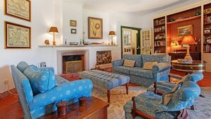 Un salon avec des canapés bleus à motifs, une table basse en bois, une cheminée et une bibliothèque.
