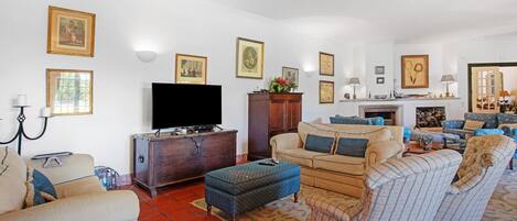 Ein Wohnzimmer mit einer Couch, einem Hocker, Sesseln, einem Fernseher und einem Kamin.