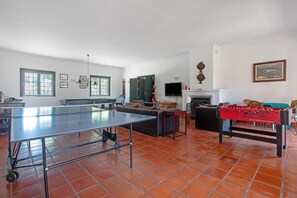 Un grand espace de vie comprenant une table de ping-pong, un baby-foot, un canapé et un téléviseur.