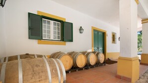 Une rangée de barils en bois est placée contre un mur percé d’une fen être et d’une porte.
