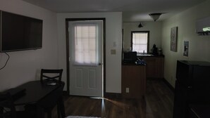 Un espacio habitable compacto con comedor, kitchenette y televisor montado en la pared.