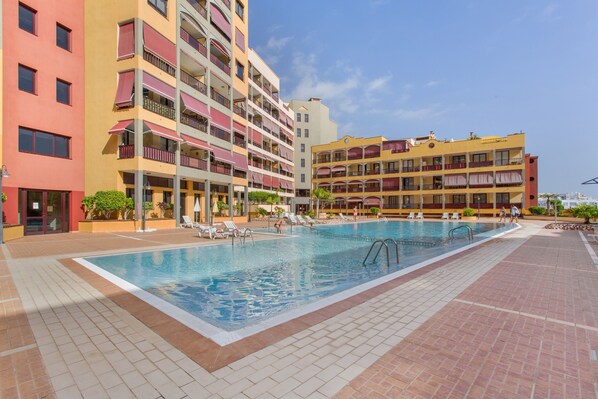 A swimming pool surrounded by multi-story buildings with balconies and a clear sky.