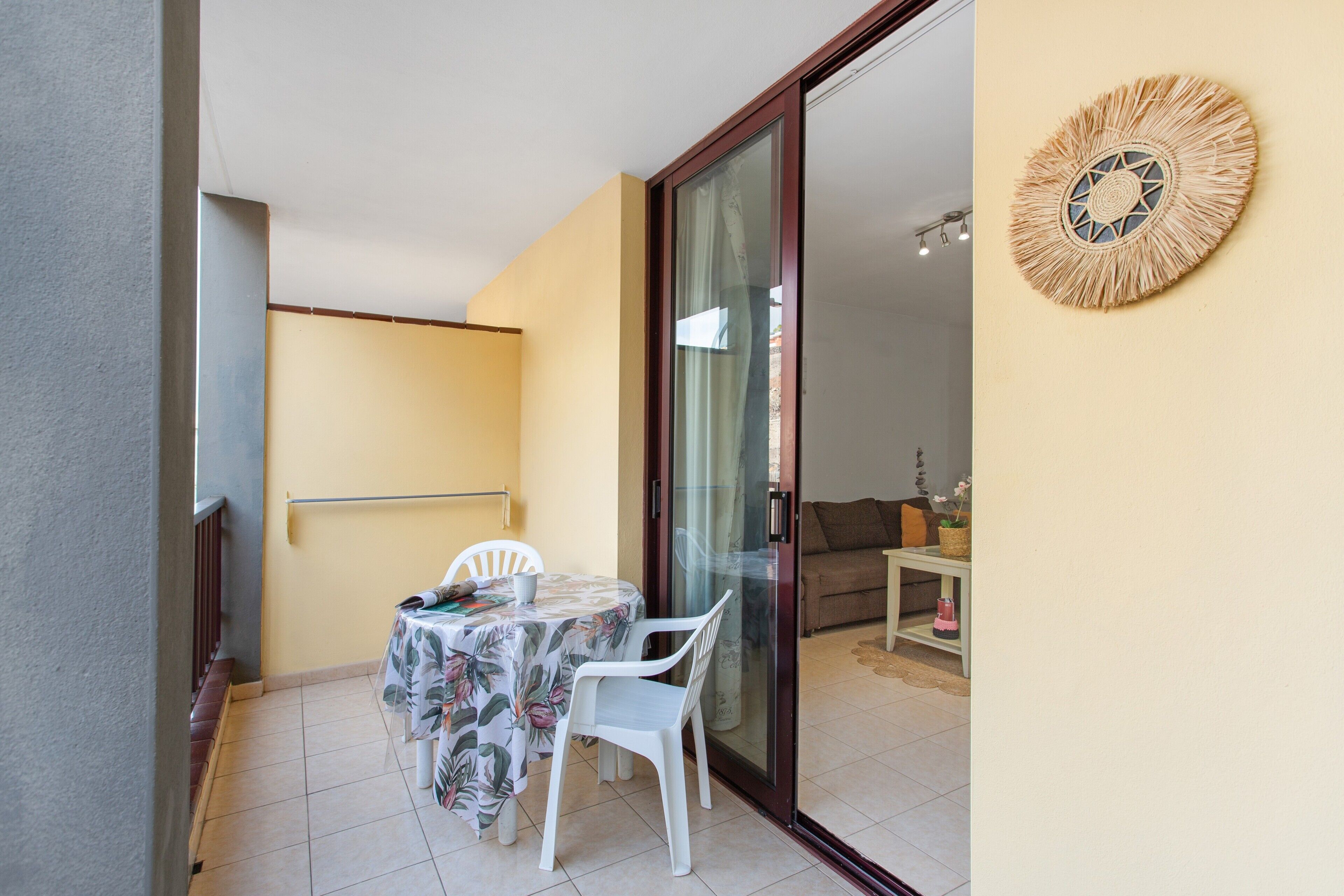 Un balcon avec une table et des chaises, une porte-fenêtre coulissante et un élément décoratif fixé au mur.