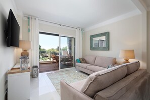 A living room with a sofa, a TV, a table with a lamp, and a view through a sliding glass door to an outdoor patio.