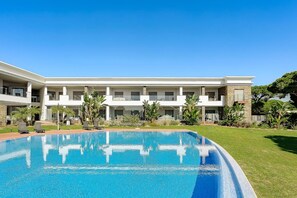 A hotel with a swimming pool, multiple balconies, and a well-maintained lawn.