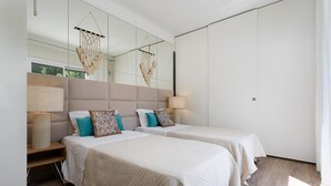 Ein modernes Schlafzimmer mit zwei Betten, einem großen Spiegel und einem Nachttisch mit einer Lampe.