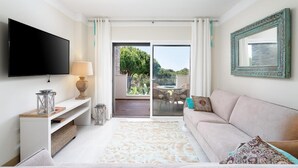 Ein Wohnzimmer mit Flachbildfernseher, einer Couch, einem Couchtisch und Blick auf eine Außenpatio mit Tisch und Stühlen.