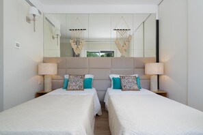 A hotel room with two beds, a large mirror, and wall-mounted lamps.