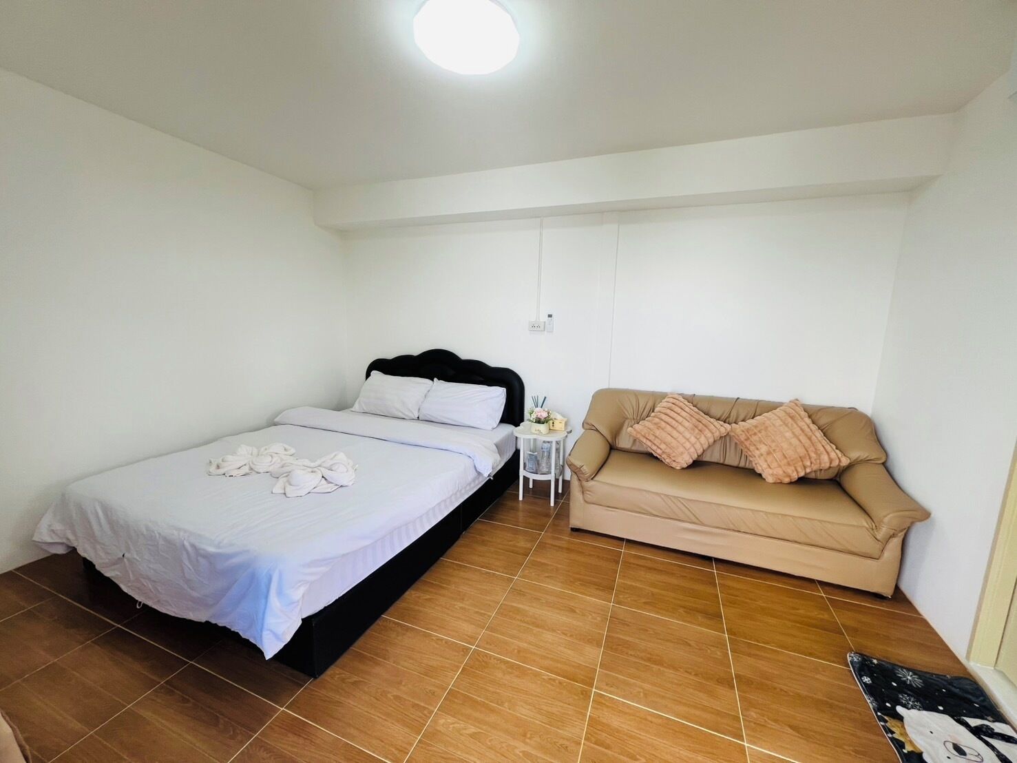 A bedroom with a bed, a sofa, a small table with a lamp, and a wall socket.