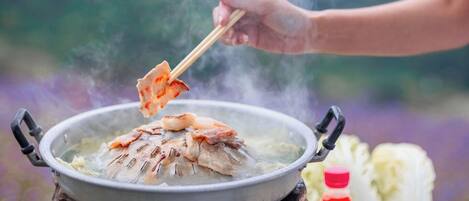 Alguém cozinha peixe numa panela sobre chama aberta, ao ar livre.