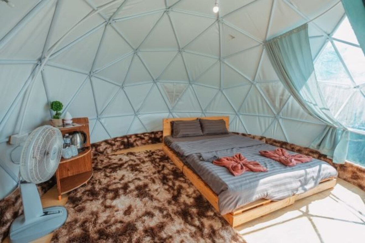 A dome-shaped room with a bed, a fan, and a small shelf with items.