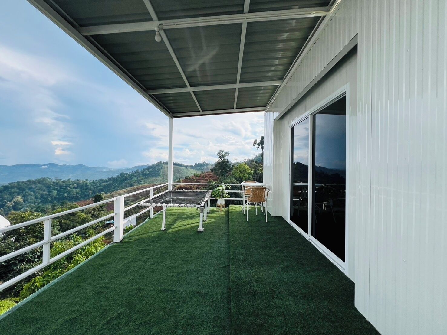 Un balcón techado con césped artificial, una mesa, sillas y vistas al campo.