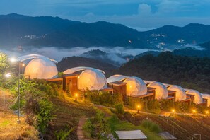 Diversas tendas em forma de cúpula com estruturas de madeira, dispostas numa encosta com vista para montanhas circundantes e um vale abaixo.