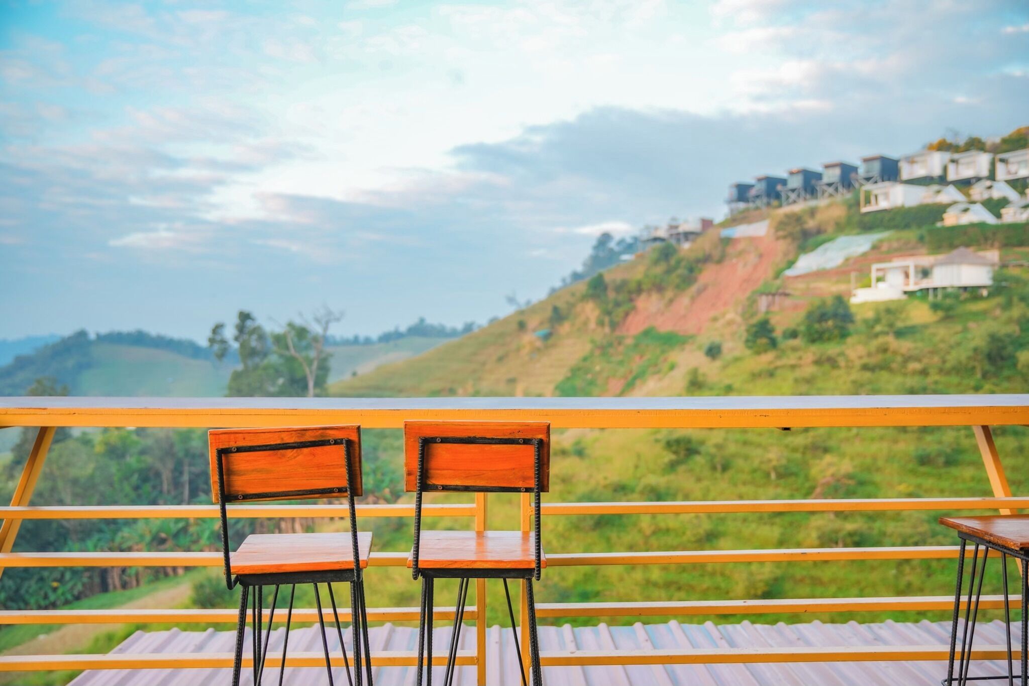 Two wooden chairs on a balcony with a view of a hillside with houses.
