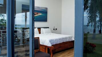 A modern bedroom with a large bed, a wooden chair, and a view of a coastal area through a glass door.