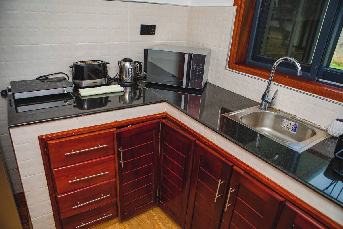 A compact kitchen with a microwave, toaster, kettle, and a sink.