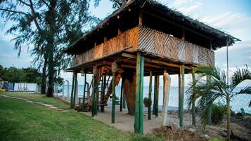 A wooden structure with a thatched roof, supported by stilts, near a body of water.